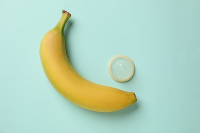 Photo of Banana and condom on turquoise background, flat lay. Safe sex concept