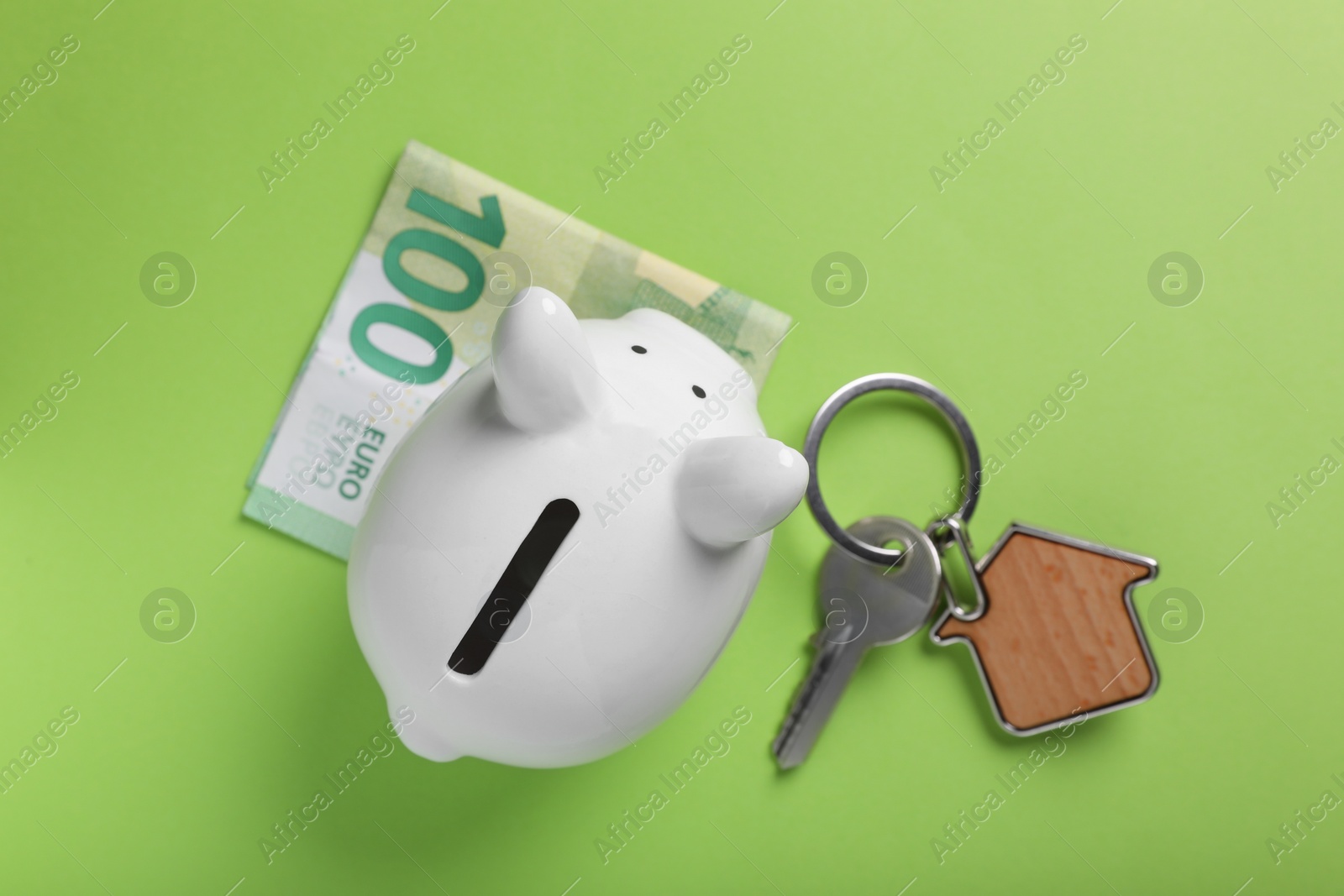 Photo of Ceramic piggy bank, euro banknote and key on light green background, flat lay. Financial savings