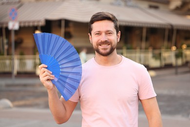 Photo of Happy man holding hand fan on city street
