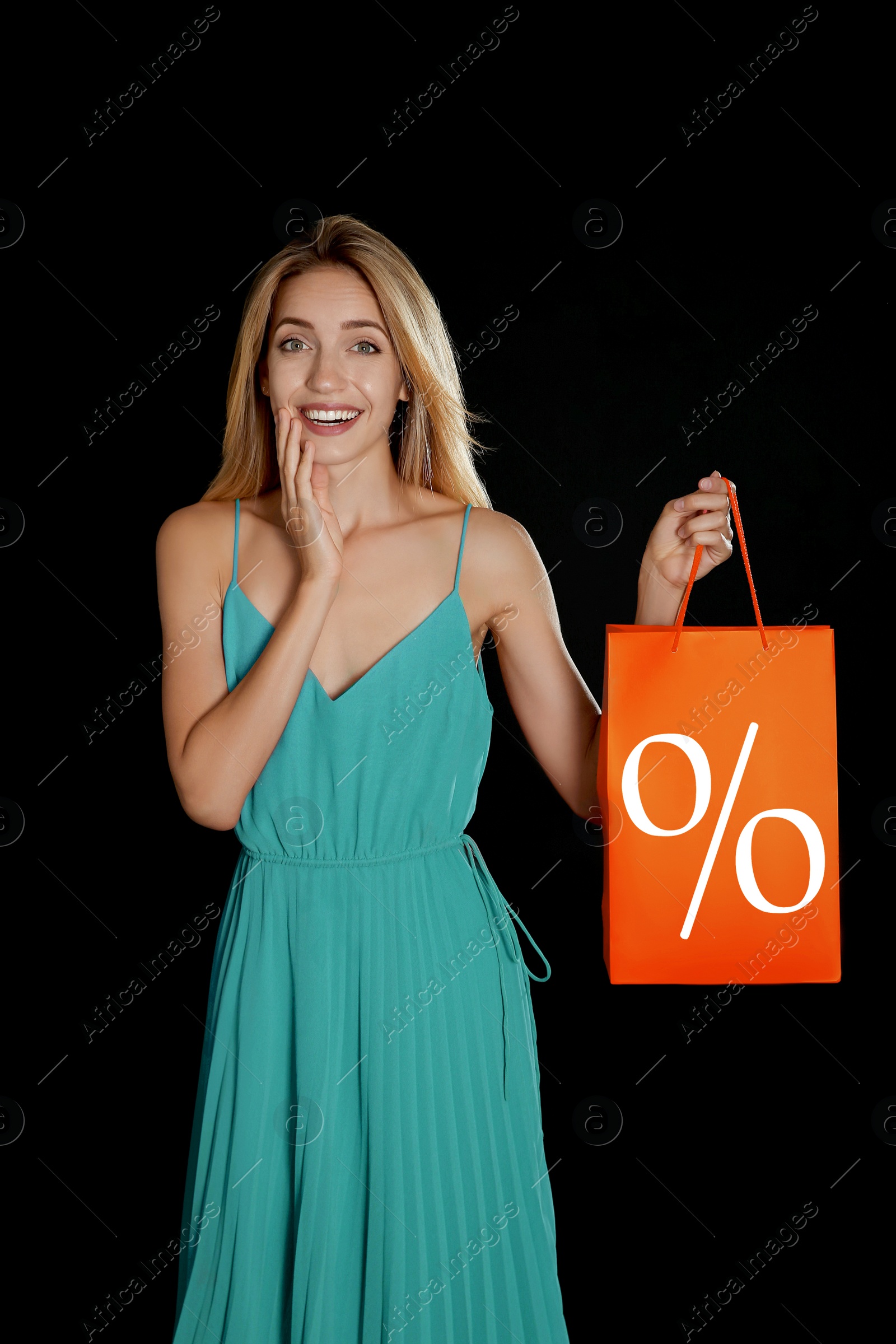 Image of Happy young woman holding shopping bag with percent sign on black background. Discount concept