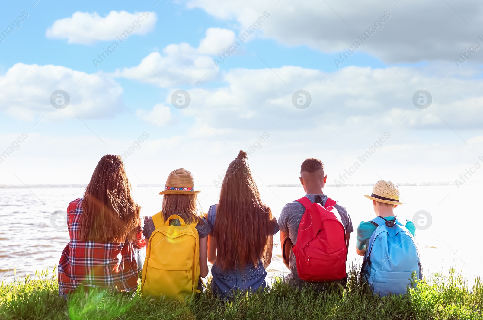 Image of School holidays. Group of children sitting on green grass near river 
