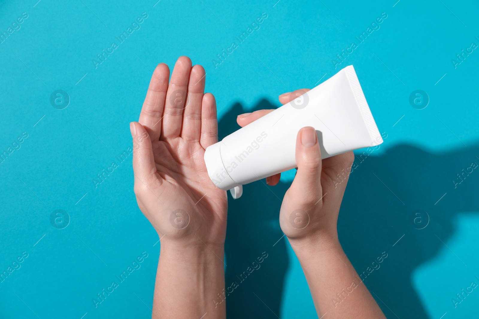 Photo of Woman with tube of hand cream on light blue background, top view