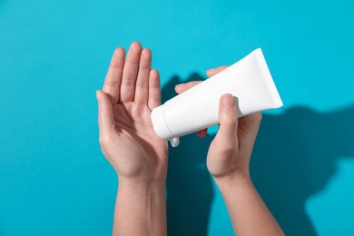 Woman with tube of hand cream on light blue background, top view