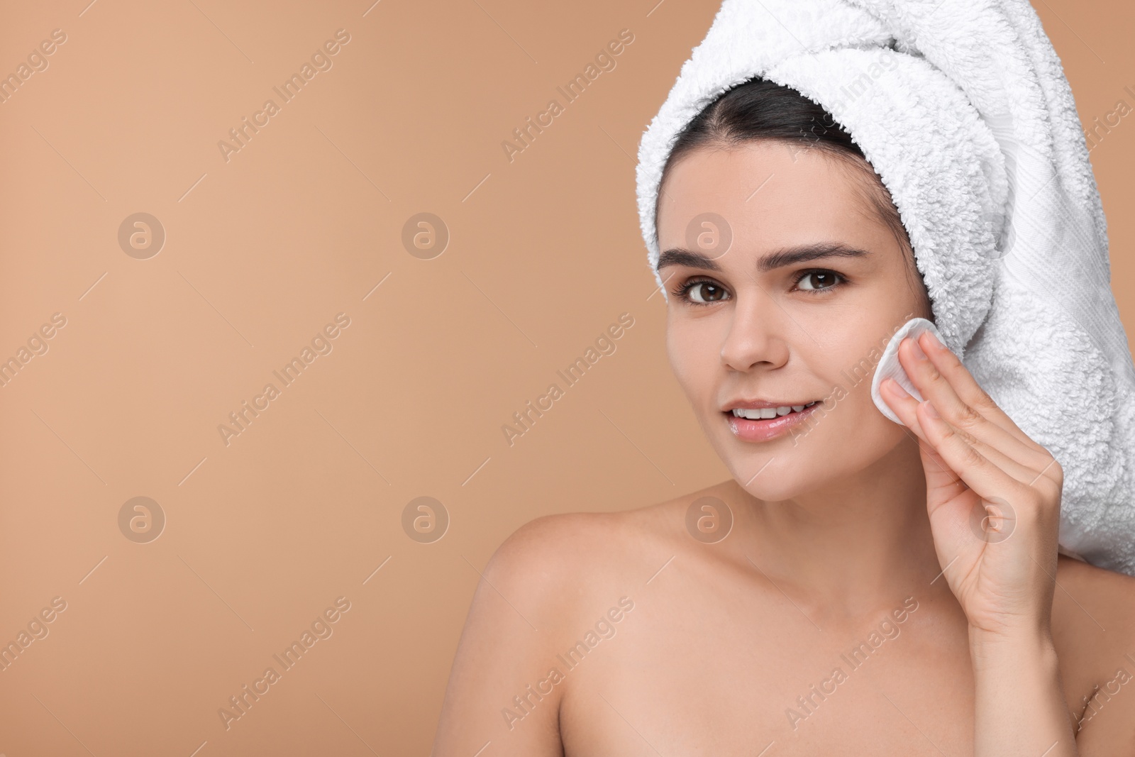 Photo of Young woman cleaning her face with cotton pad on beige background. Space for text