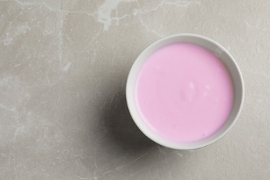 Photo of Bowl with delicious organic yogurt on grey marble table, top view. Space for text