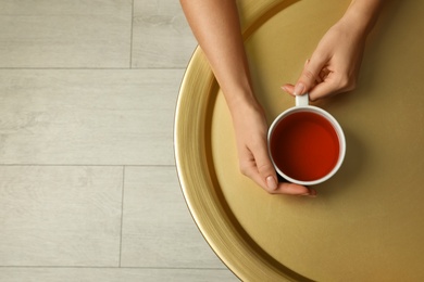 Woman with cup of black tea at golden table indoors, top view. Space for text