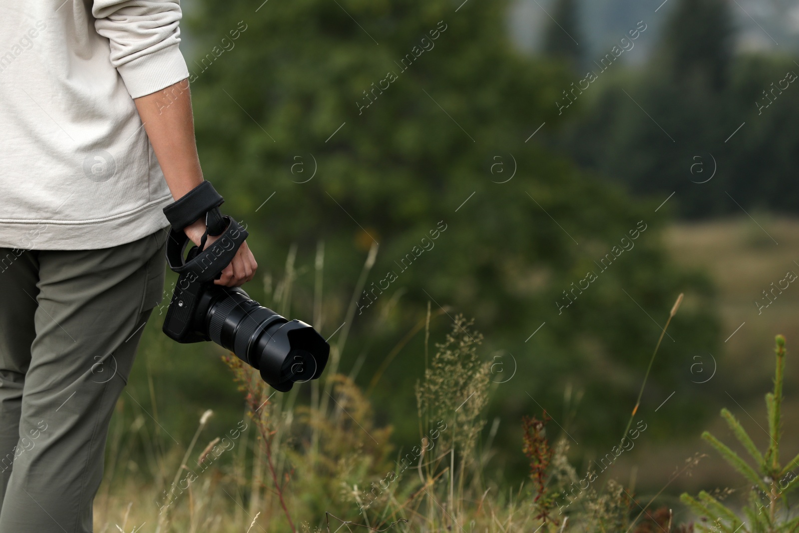 Photo of Photographer holding modern camera outdoors, closeup. Space for text