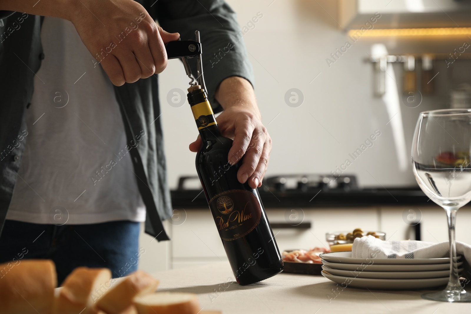 Photo of Man opening wine bottle with corkscrew at table indoors, closeup