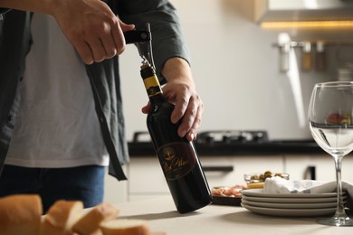 Photo of Man opening wine bottle with corkscrew at table indoors, closeup