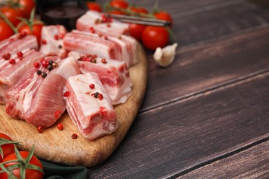 Photo of Cut raw pork ribs with peppercorns on wooden table, closeup. Space for text