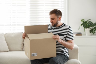 Photo of Happy young man opening parcel at home