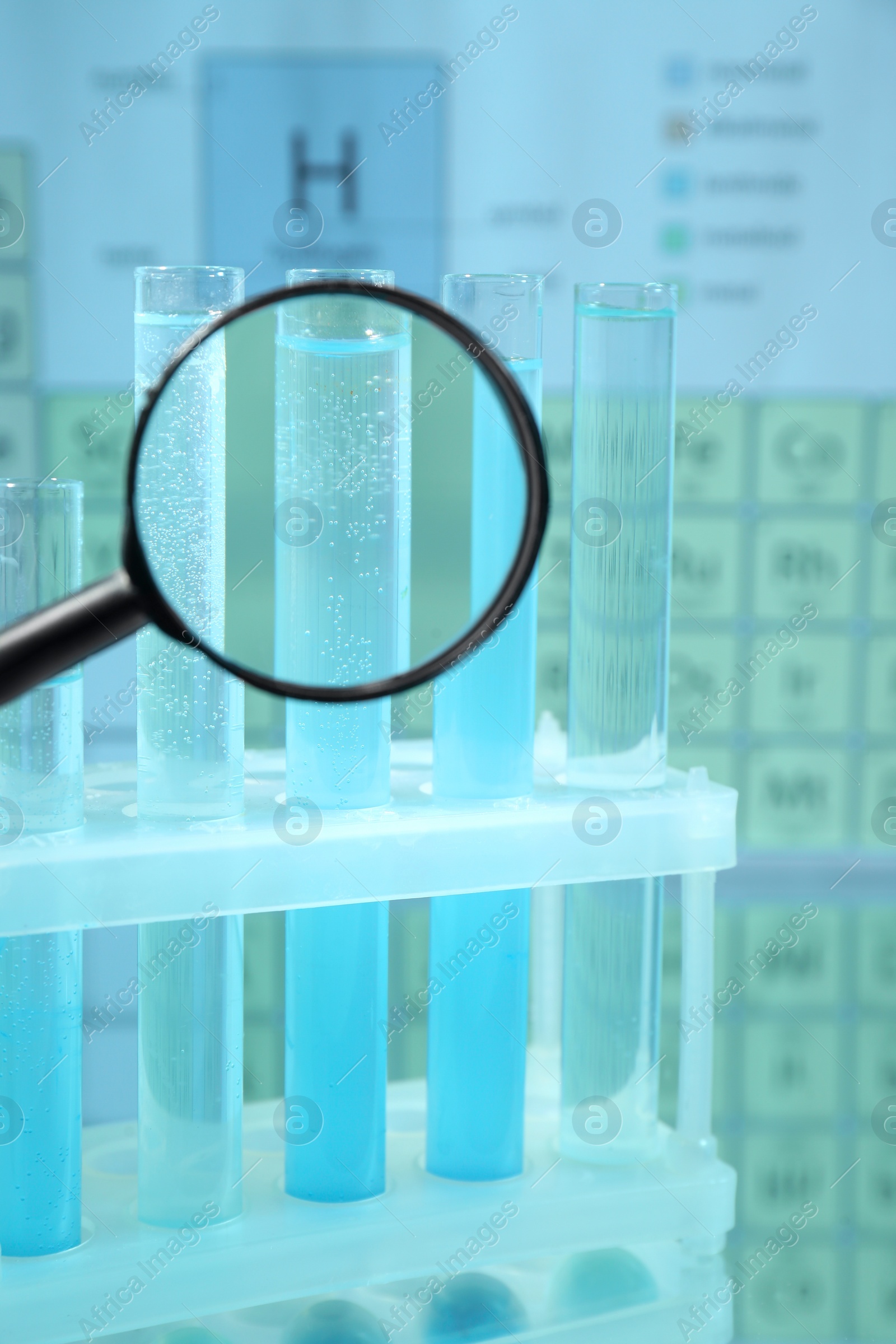 Photo of Magnifying glass and test tubes in rack on mirror surface against periodic table of chemical elements