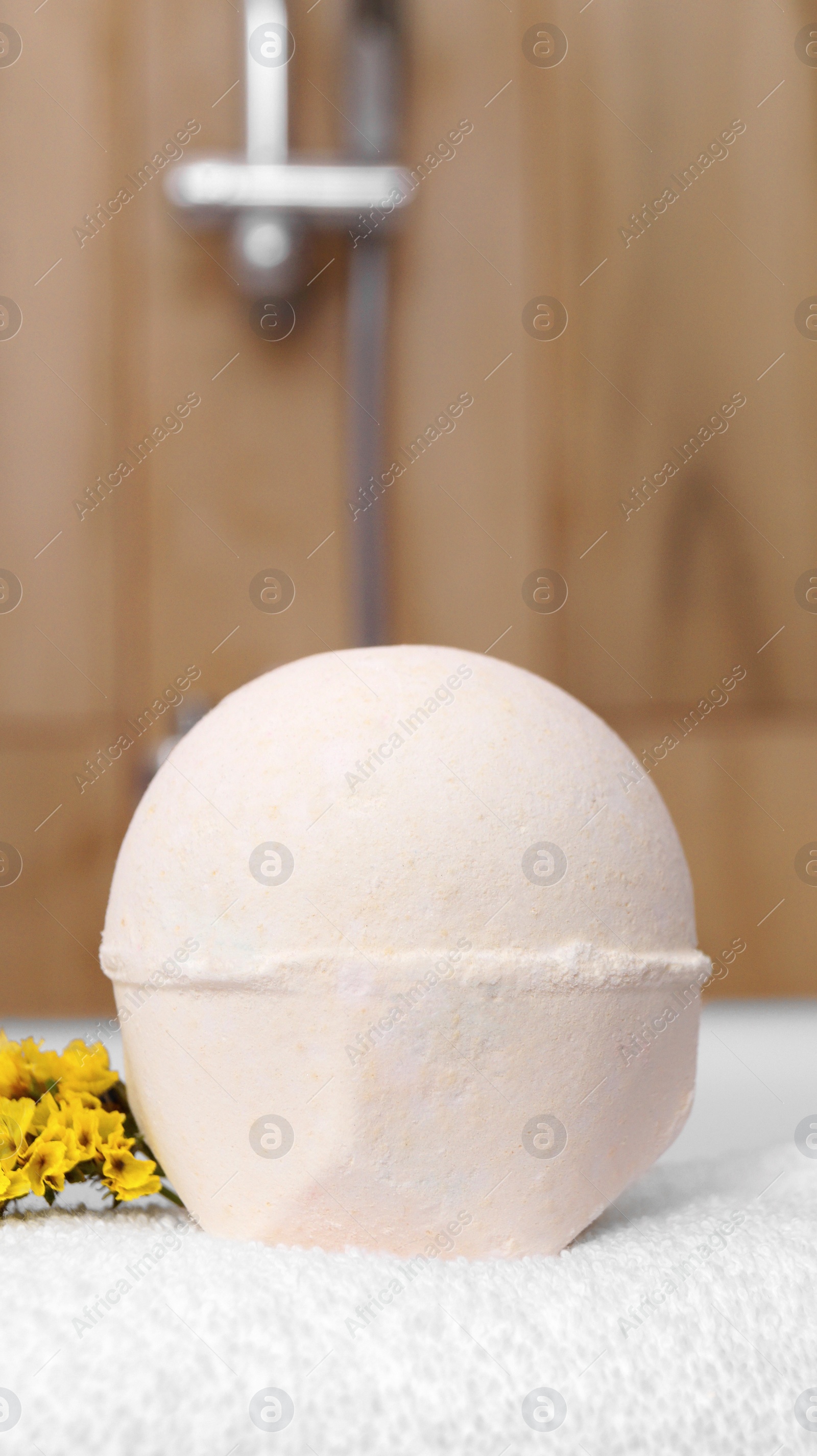 Photo of Towel with bath bomb and flowers on tub indoors, closeup