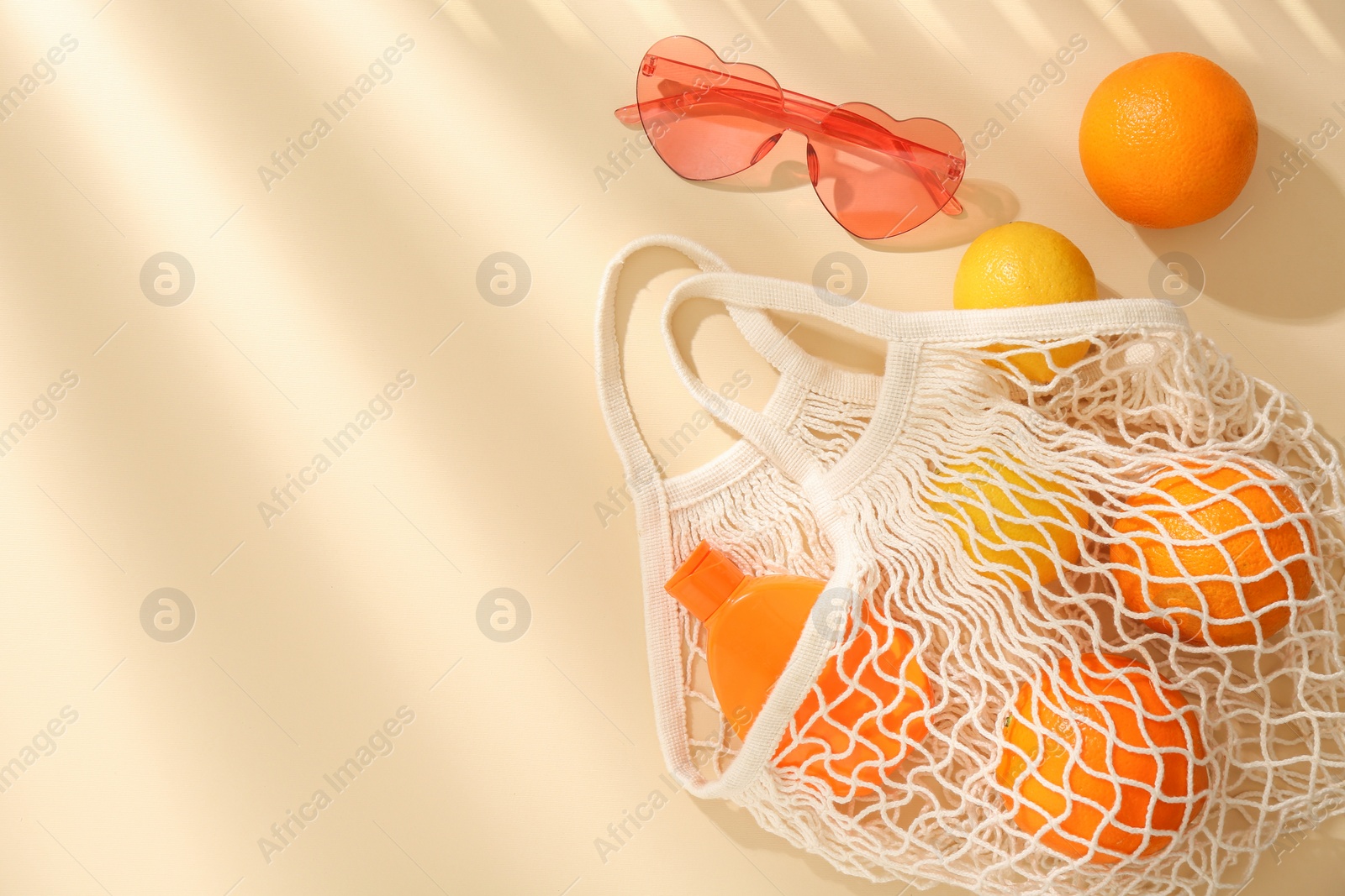 Photo of String bag with fresh fruits, sunscreen and sunglasses on beige background, flat lay. Space for text