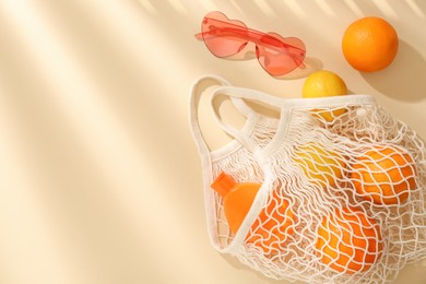 String bag with fresh fruits, sunscreen and sunglasses on beige background, flat lay. Space for text