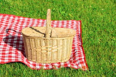 Picnic basket with checkered tablecloth on green grass outdoors