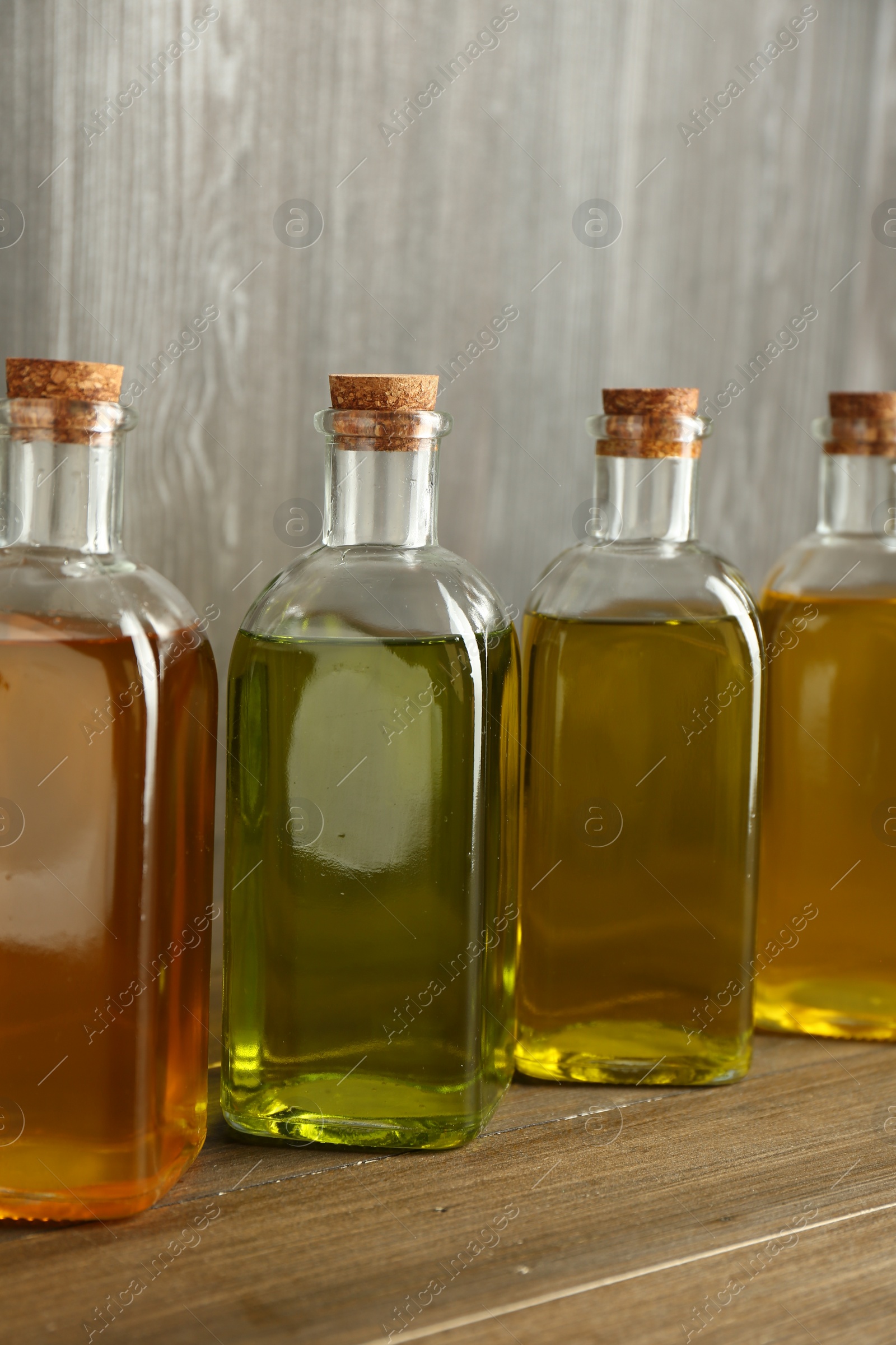 Photo of Vegetable fats. Different oils in glass bottles on wooden table, closeup