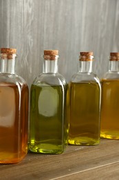 Photo of Vegetable fats. Different oils in glass bottles on wooden table, closeup