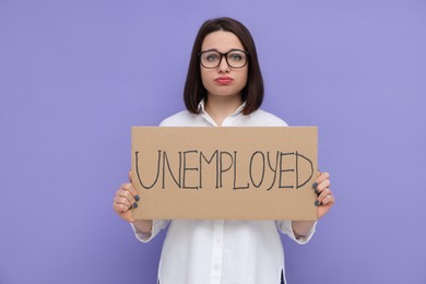 Photo of Young woman holding sign with word Unemployed on violet background