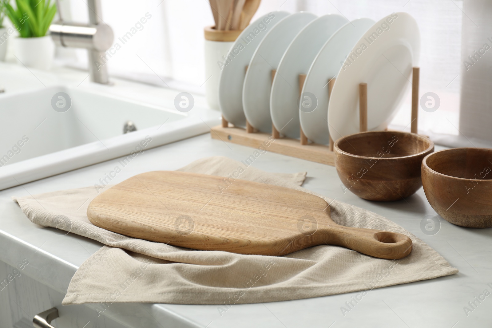 Photo of Wooden cutting board, dishware and towel on white countertop in kitchen