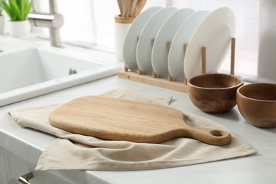 Wooden cutting board, dishware and towel on white countertop in kitchen