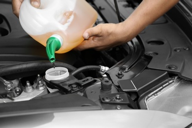 Man pouring liquid from plastic canister into car washer fluid reservoir, closeup