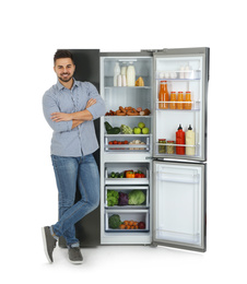 Young man near open refrigerator on white background