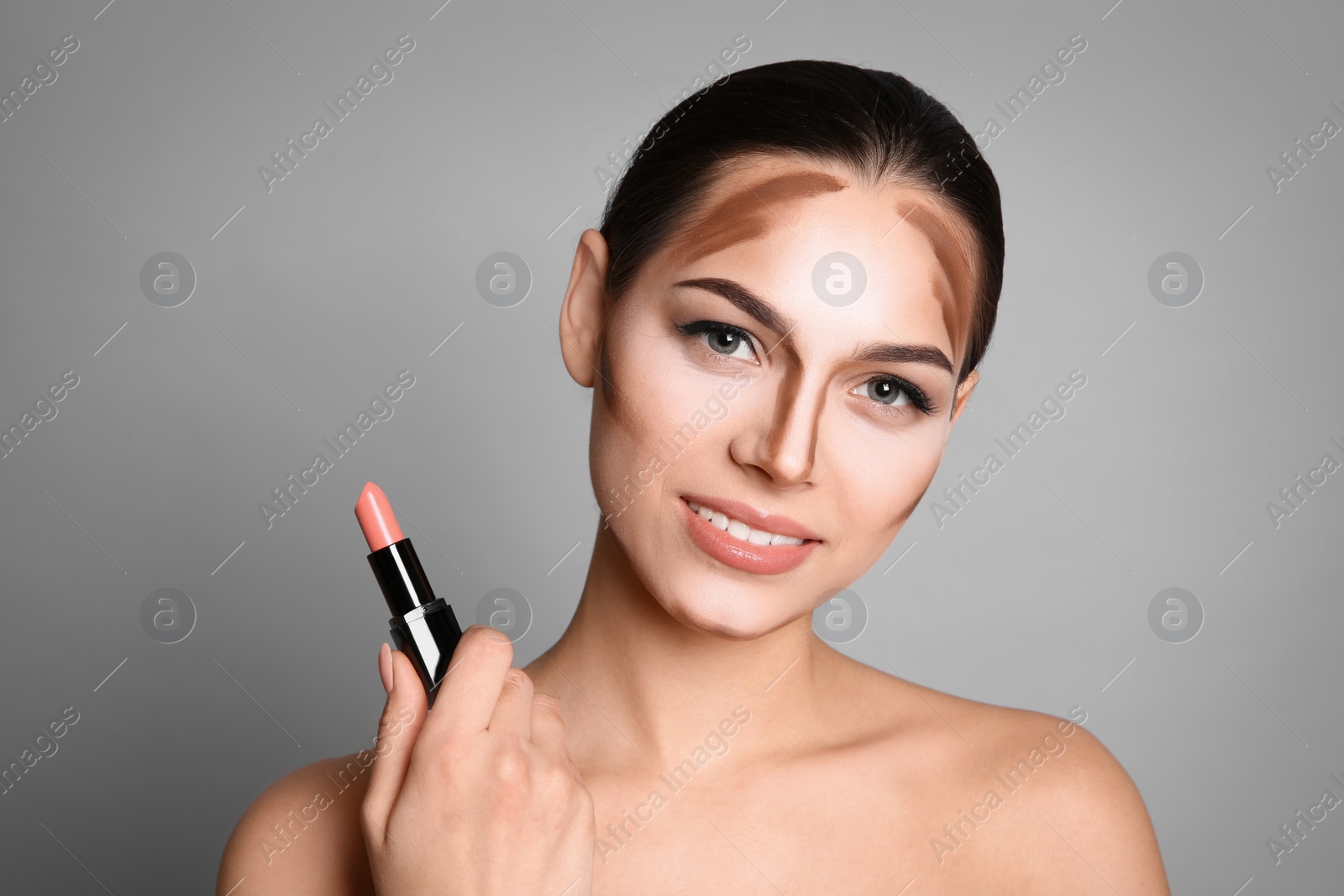 Photo of Young woman with contouring lines on her face against grey background. Professional makeup products