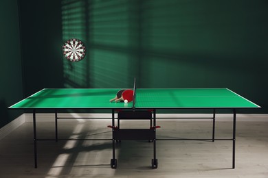 Photo of Green ping pong table with rackets and ball indoors