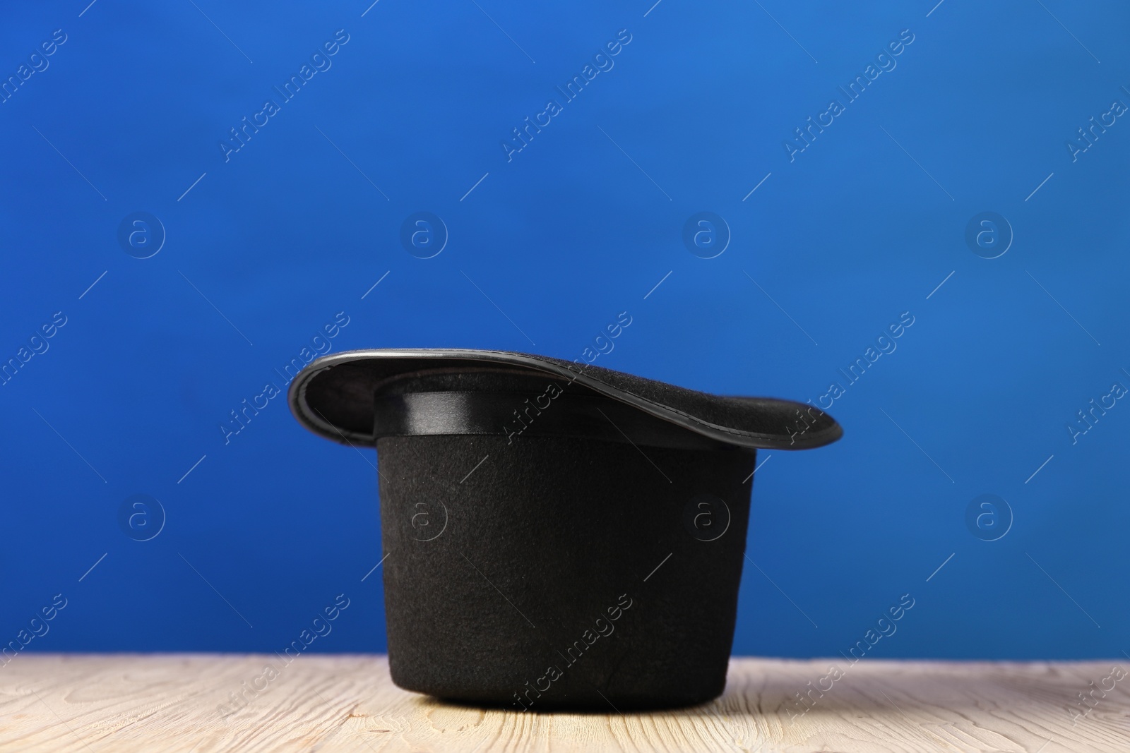 Photo of Magician's hat on wooden table against blue background