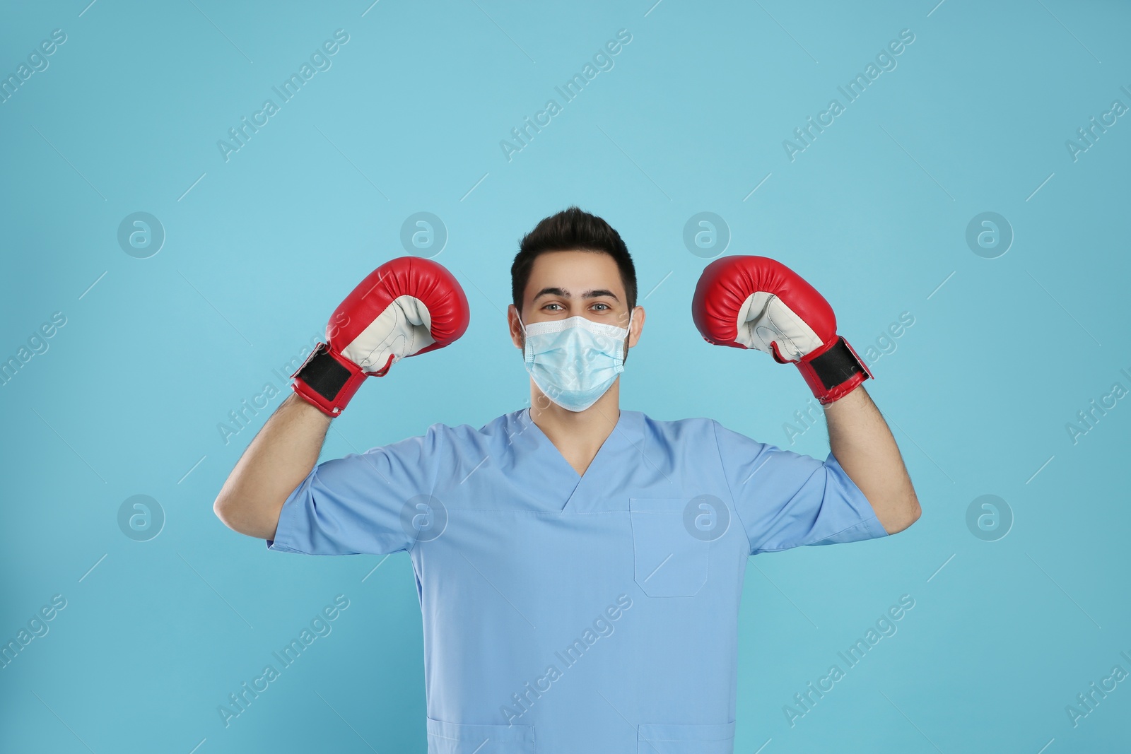 Photo of Doctor with protective mask and boxing gloves on light blue background. Strong immunity concept