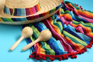 Photo of Mexican sombrero hat, maracas and colorful poncho on light blue background