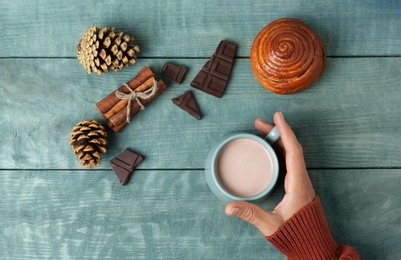 Photo of Woman with cup of delicious cocoa drink at light blue wooden table, top view