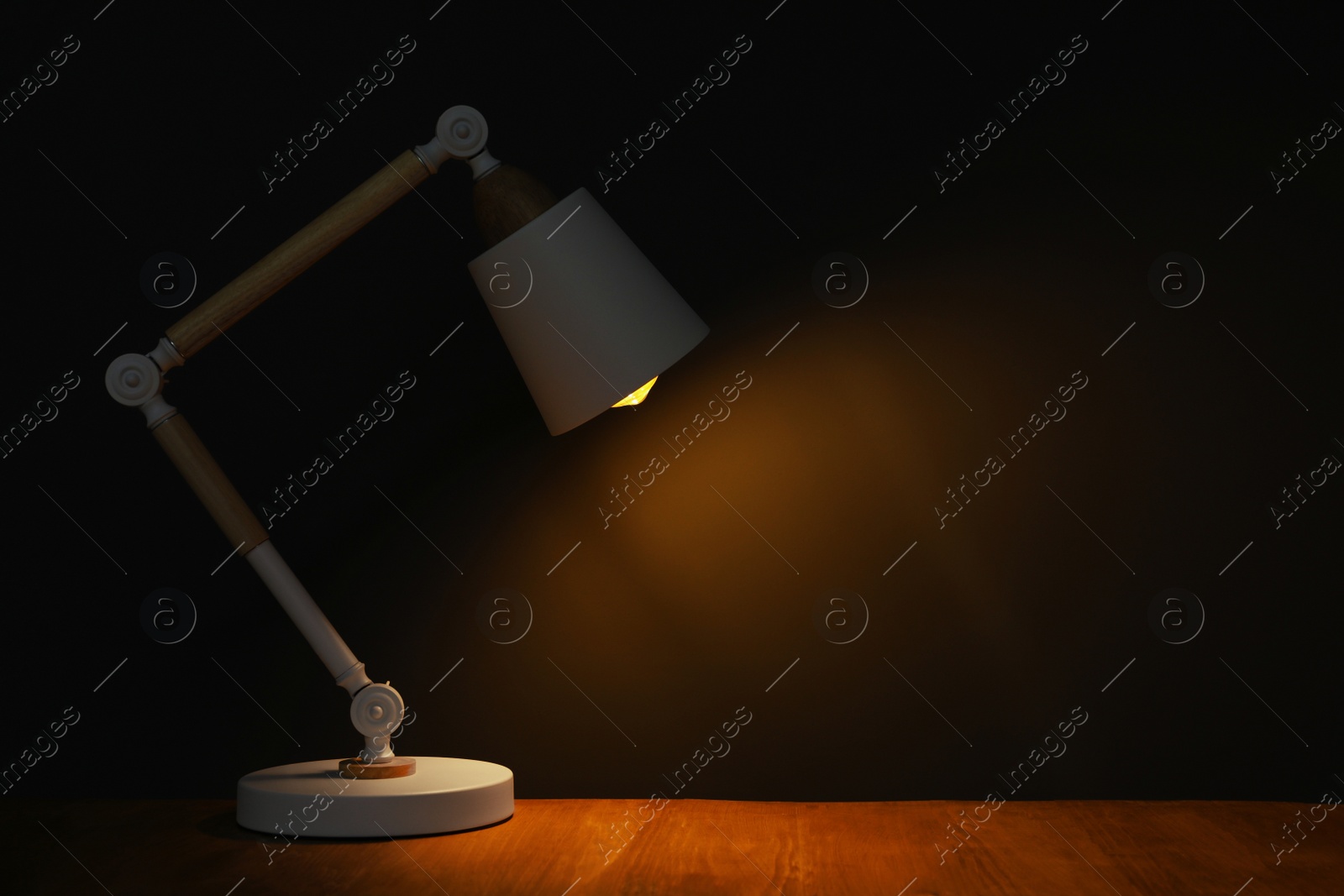 Photo of Stylish modern desk lamp on wooden table at night, space for text