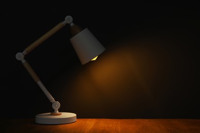 Photo of Stylish modern desk lamp on wooden table at night, space for text