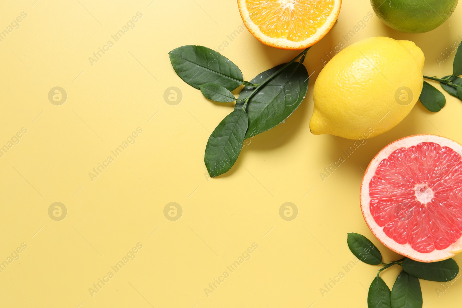 Photo of Different cut and whole citrus fruits on yellow table, flat lay. Space for text