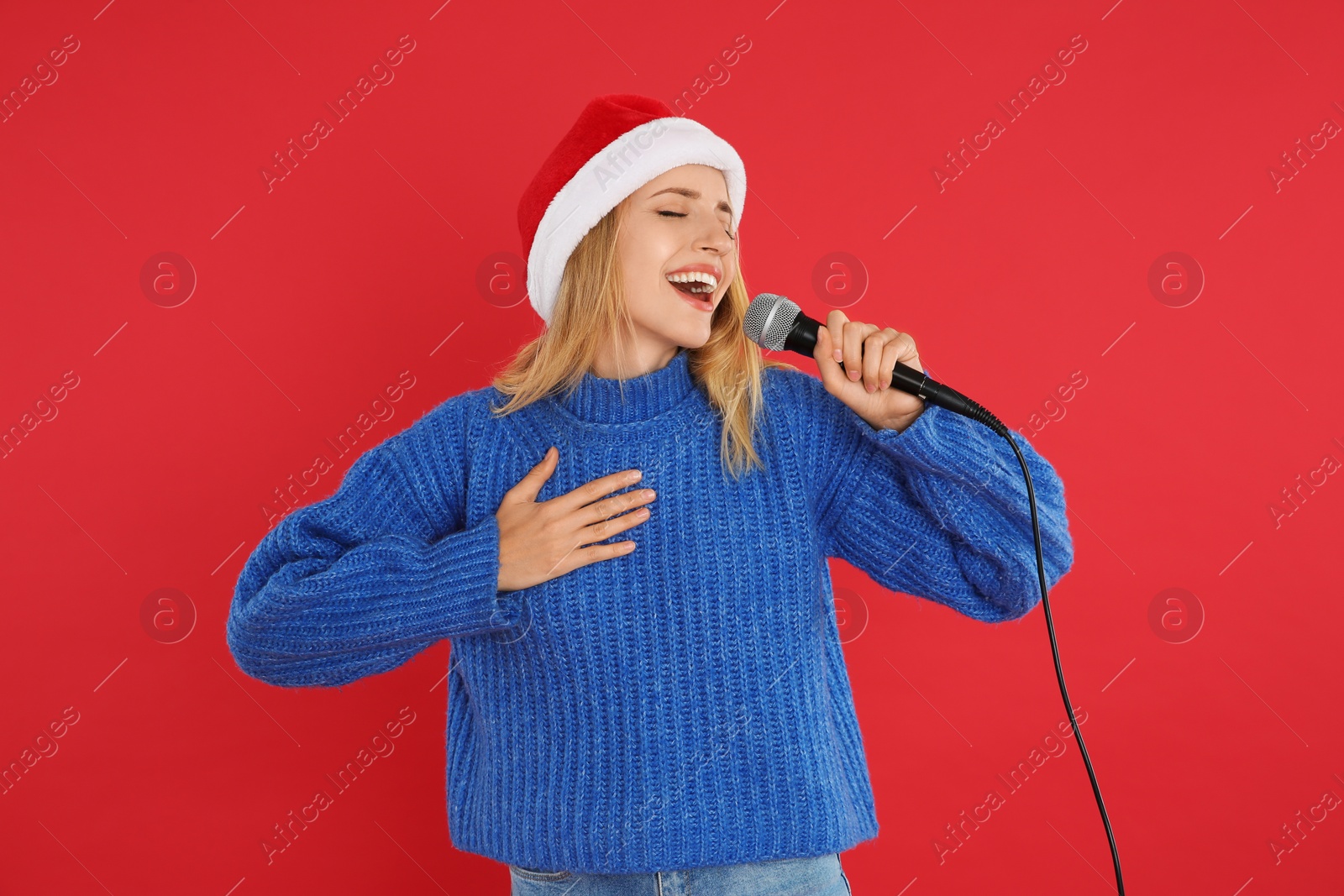 Photo of Happy woman in Santa Claus hat singing with microphone on red background. Christmas music