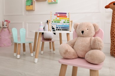 Photo of Cute toy bear on small chair in playroom. Interior design