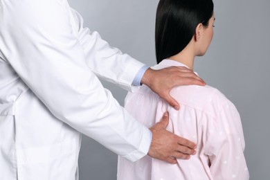 Doctor examining woman with shoulder pain on grey background