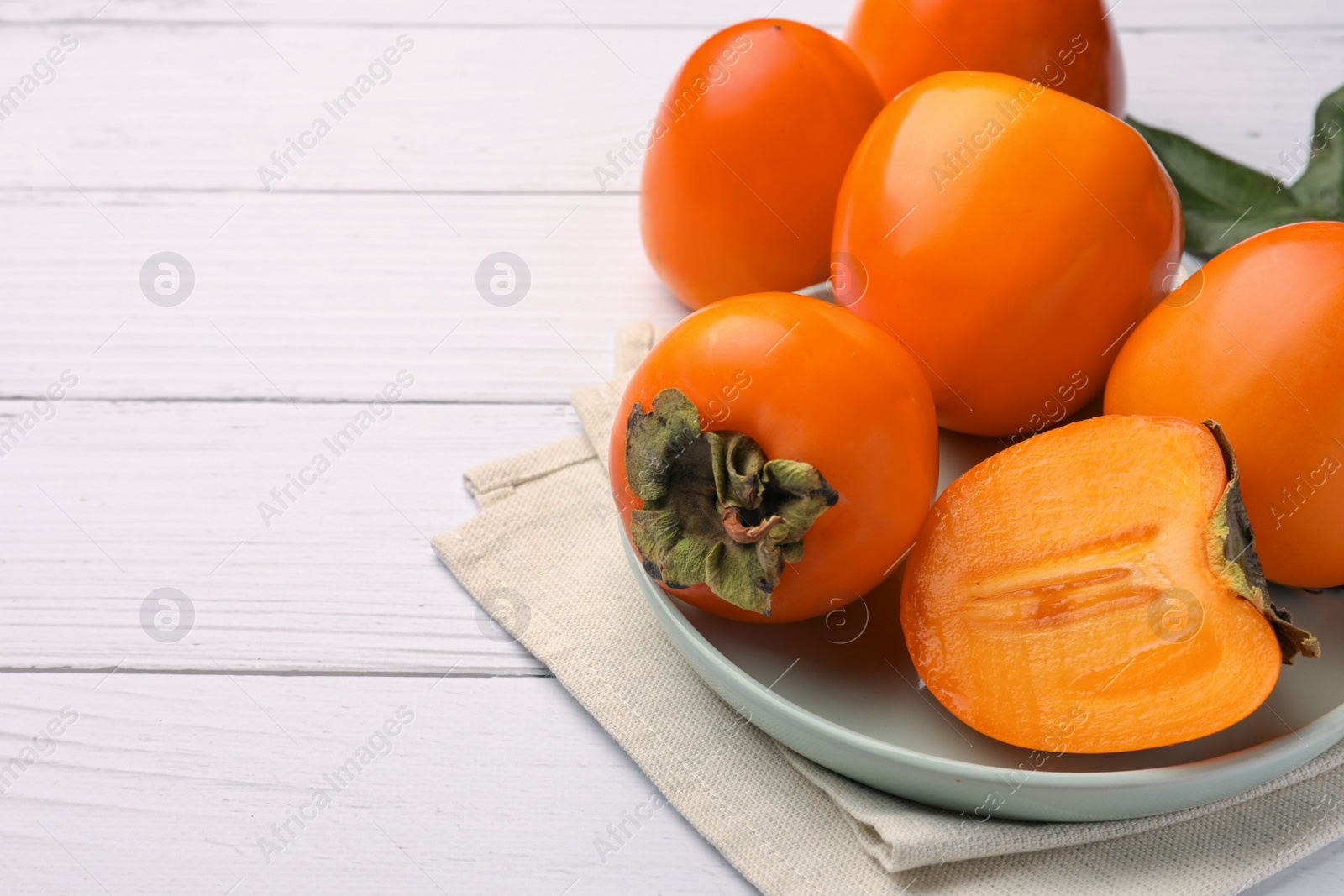 Photo of Delicious ripe juicy persimmons on white wooden table, space for text
