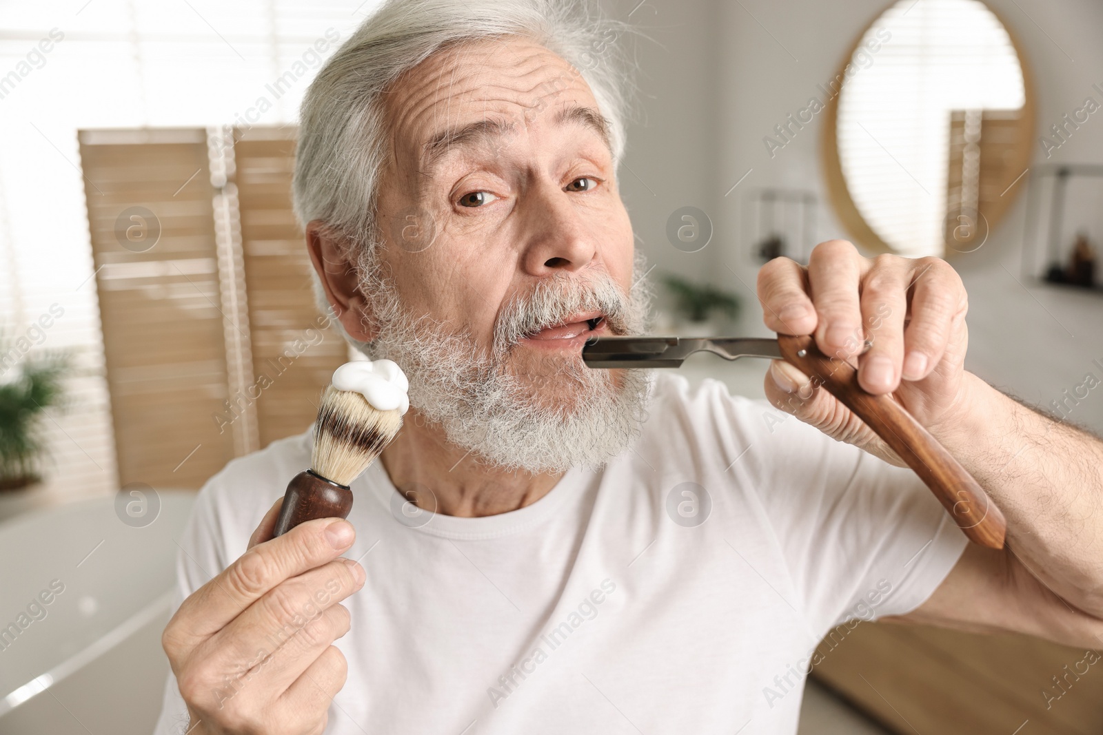 Photo of Man shaving mustache and beard with blade in bathroom