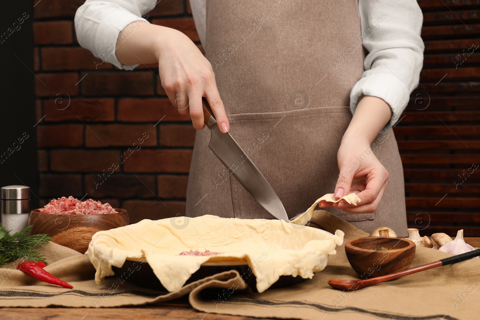 Photo of Woman cutting dough leftovers for meat pie in baking dish at table, closeup