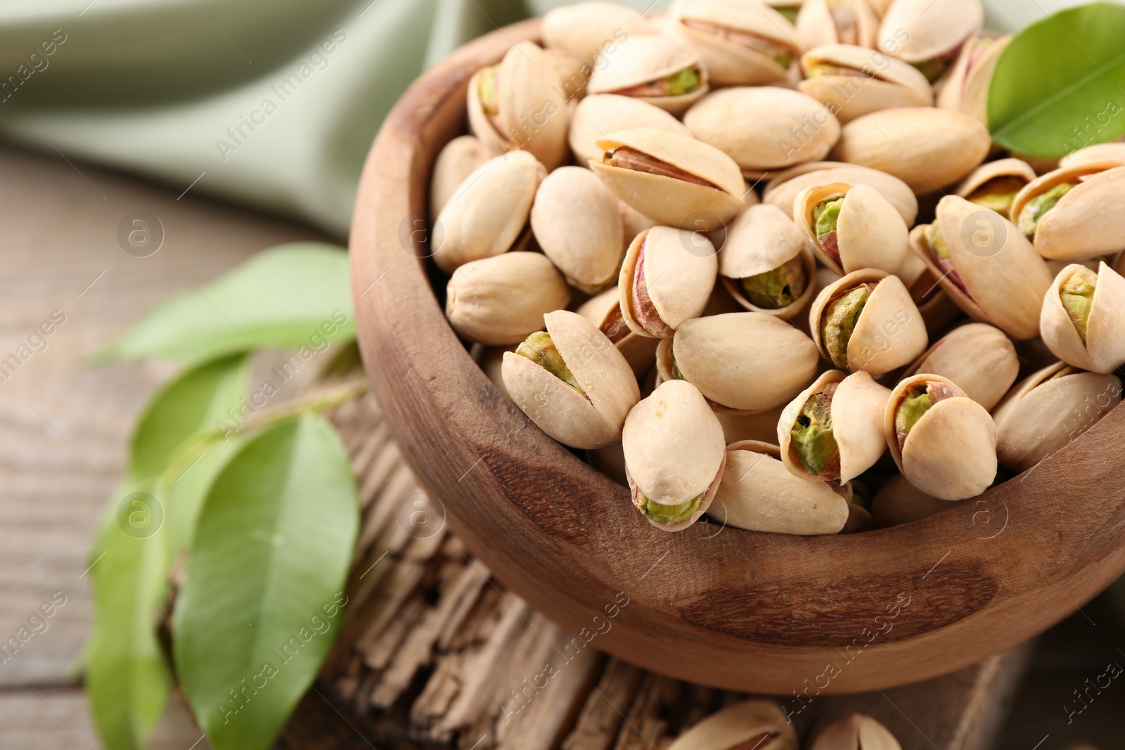 Photo of Delicious pistachios in bowl on wooden table, closeup