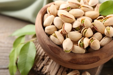 Photo of Delicious pistachios in bowl on wooden table, closeup