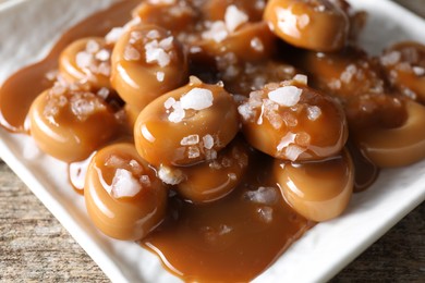 Photo of Tasty candies, caramel sauce and salt on wooden table, closeup