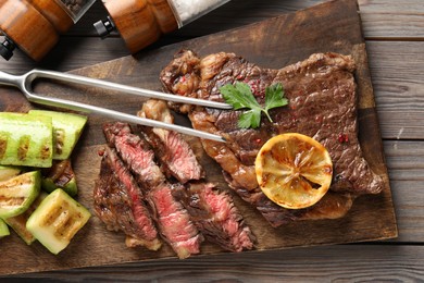 Photo of Delicious grilled beef steak and vegetables served on wooden table, top view