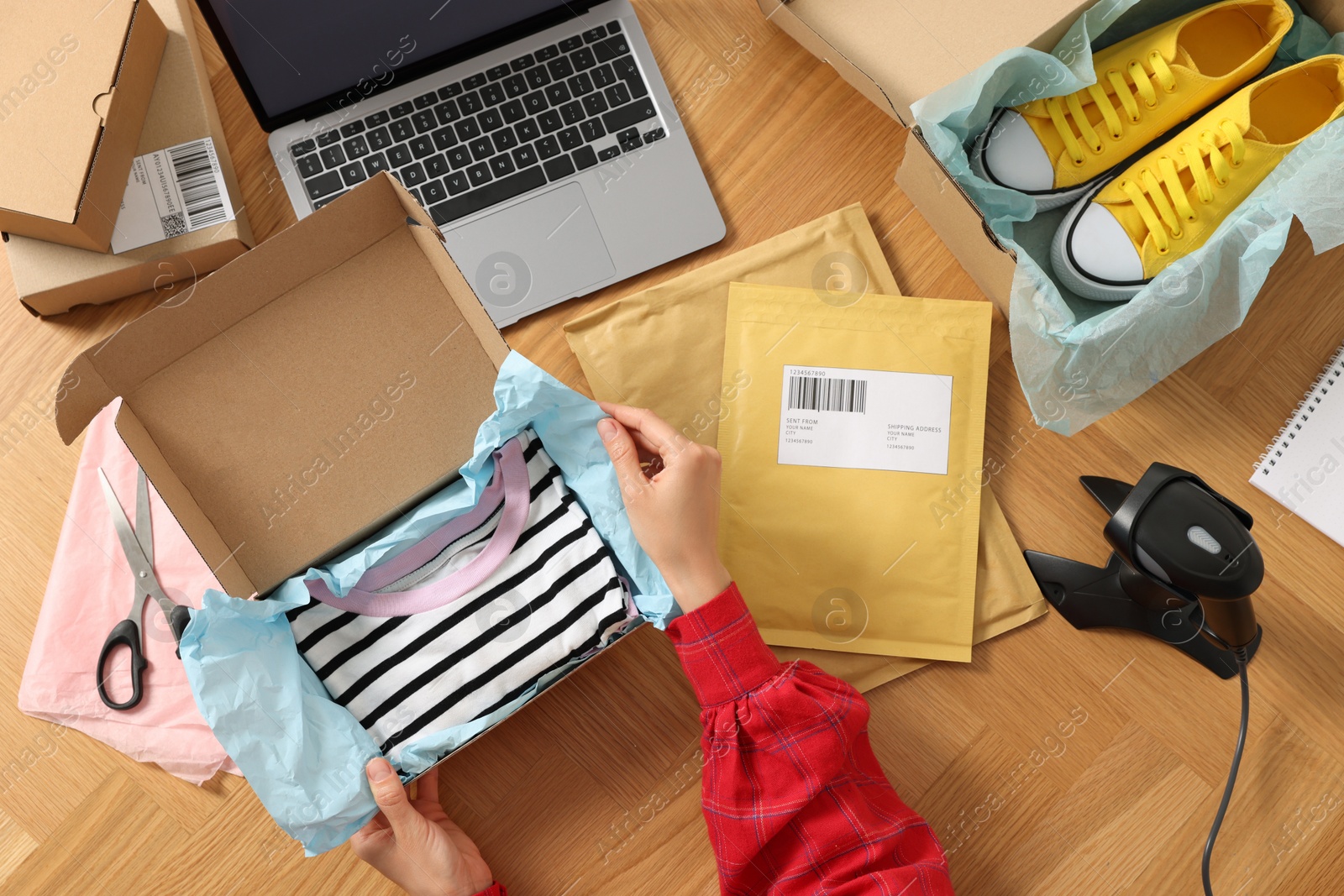 Photo of Woman packing clothes at wooden table, top view. Online store