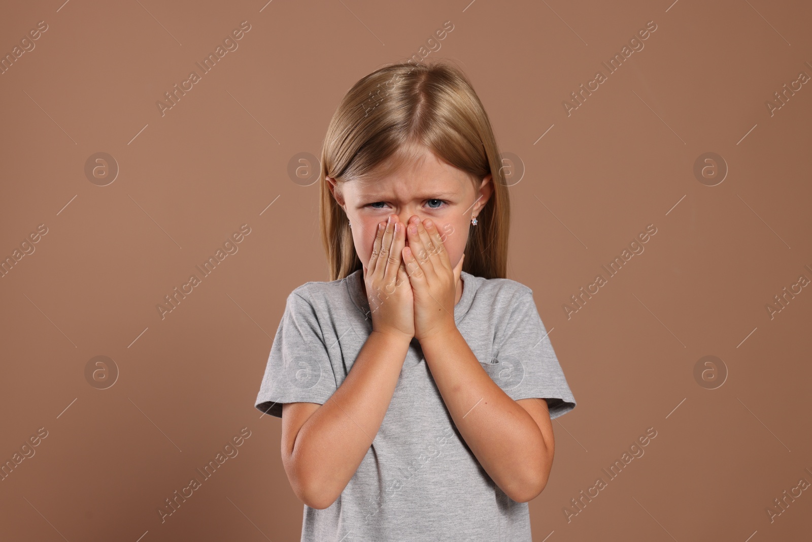 Photo of Suffering from allergy. Little girl sneezing on light brown background