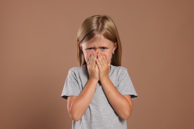 Photo of Suffering from allergy. Little girl sneezing on light brown background