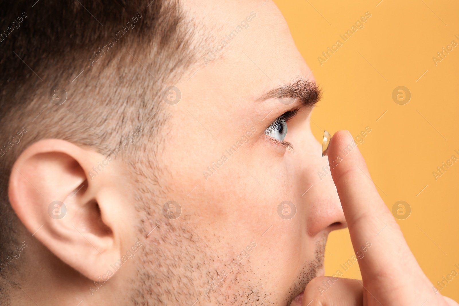 Photo of Young man putting contact lens in his eye on color background